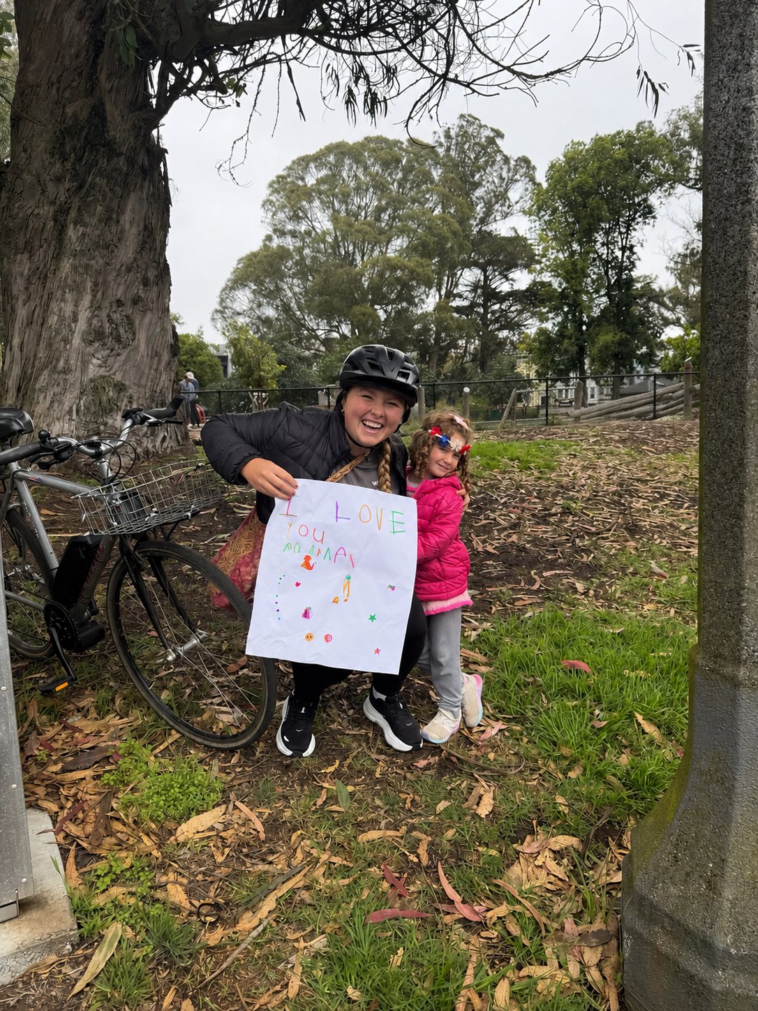 Olivia smiling outdoors with a young participant holding a handmade drawing