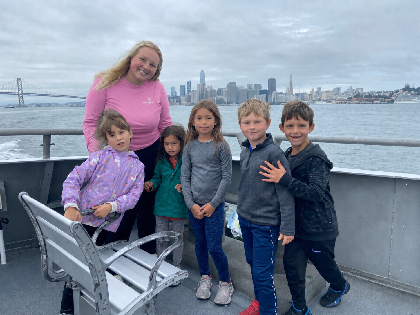 Olivia and a small group of children smiling together on a ferry with the San Francisco skyline in the background